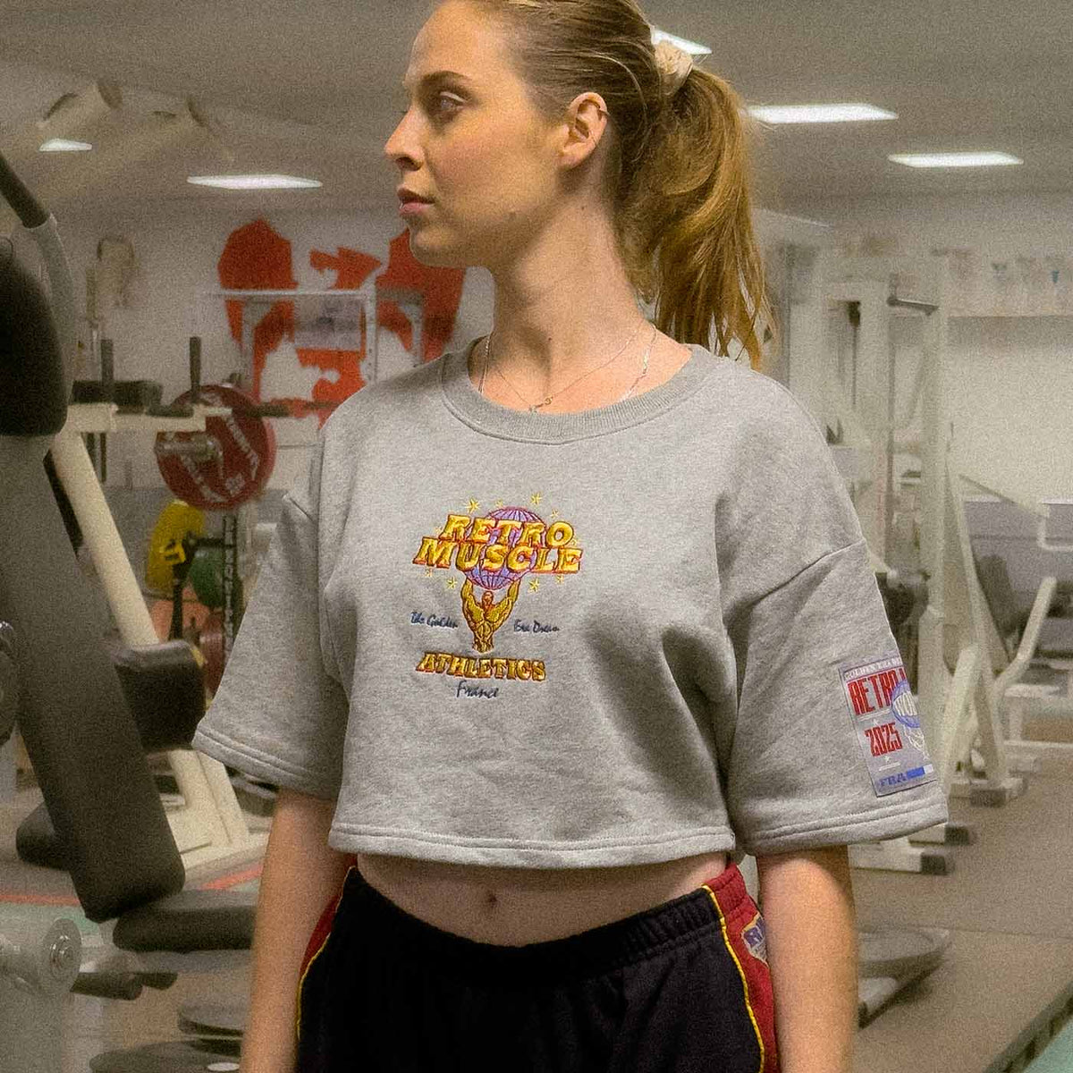 Modèle portant un sweat RetroMuscle gris dans une salle de sport